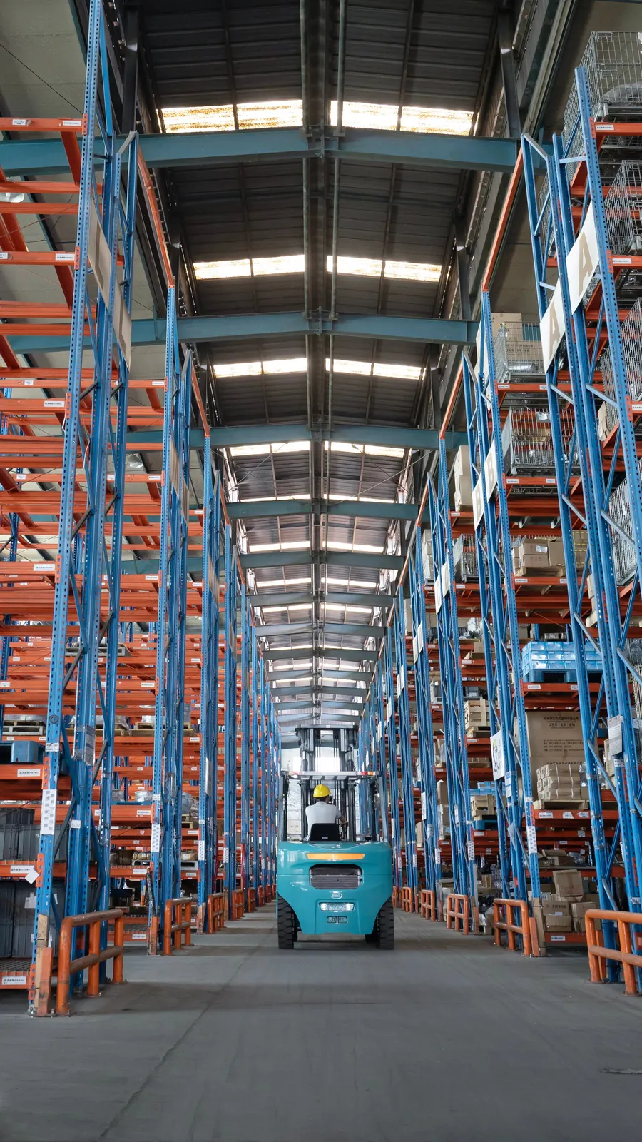 Xe nâng điện Baoli KBE40-X — chạy giữa hai dãy kệ cao
